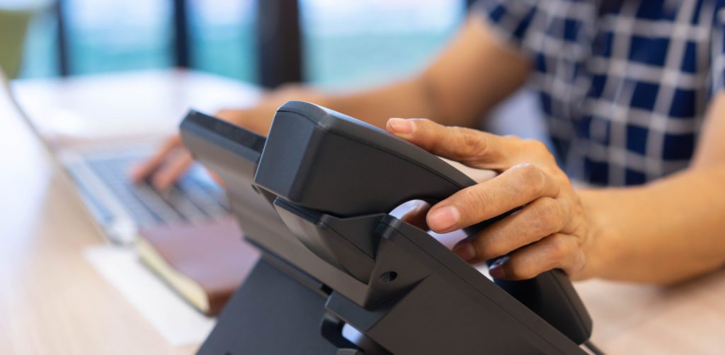 close up senior woman hand touching on handset telephone to calling to colleagues or answering ringing call from customer at office for communication and contact us concept
